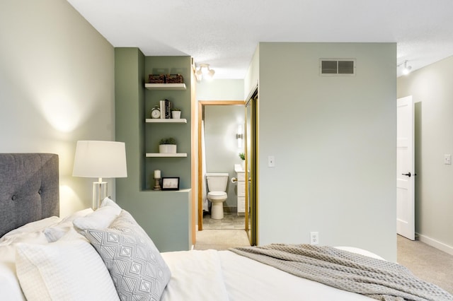 bedroom with light colored carpet, visible vents, rail lighting, ensuite bathroom, and baseboards