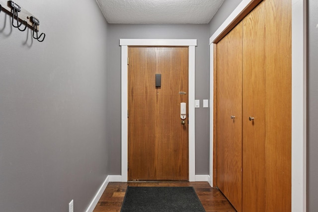 doorway with a textured ceiling, baseboards, and dark wood-type flooring