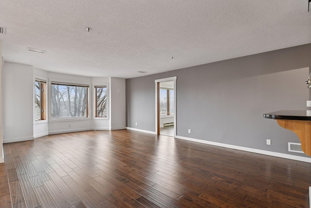 unfurnished living room featuring dark wood finished floors, visible vents, a baseboard heating unit, a textured ceiling, and baseboards