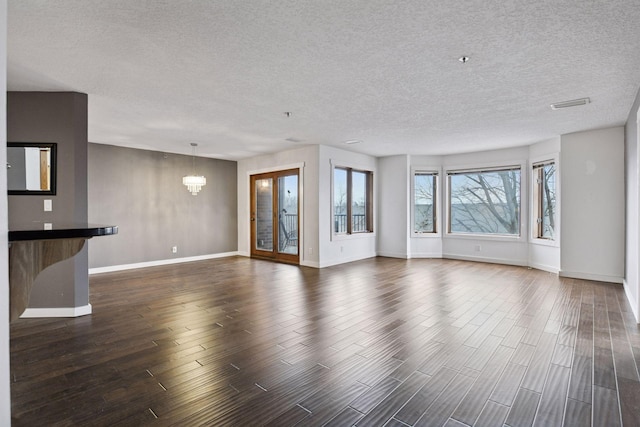 unfurnished living room featuring dark wood-style floors, visible vents, a textured ceiling, a chandelier, and baseboards