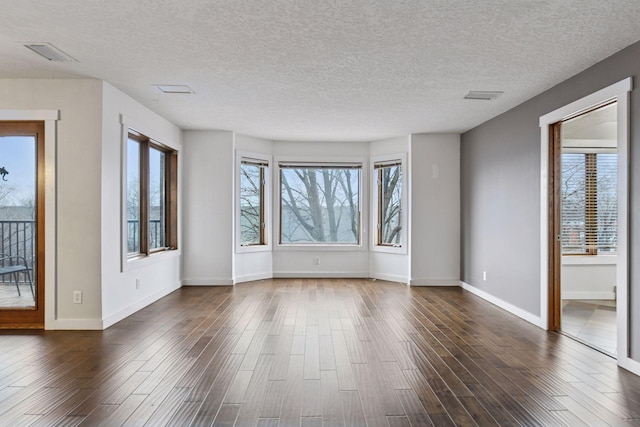 unfurnished room featuring dark wood finished floors, visible vents, and baseboards