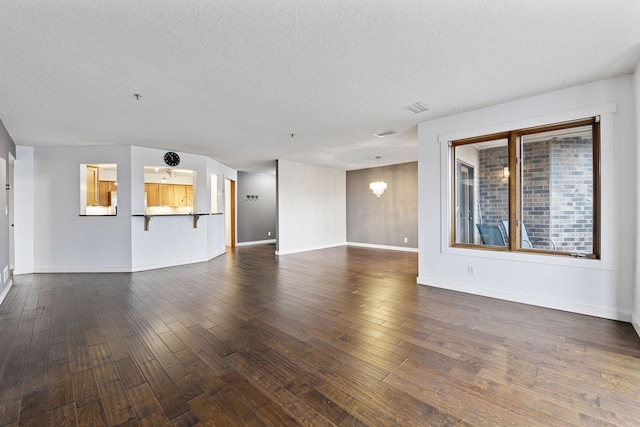 unfurnished living room featuring dark wood-style floors, visible vents, a textured ceiling, and baseboards