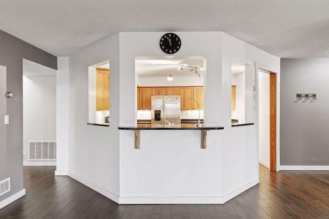 kitchen featuring dark wood-style floors, stainless steel refrigerator with ice dispenser, dark countertops, visible vents, and baseboards