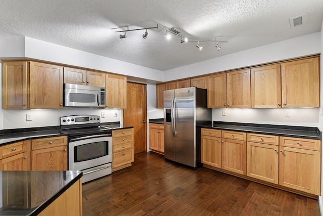 kitchen with a textured ceiling, visible vents, appliances with stainless steel finishes, dark countertops, and dark wood finished floors