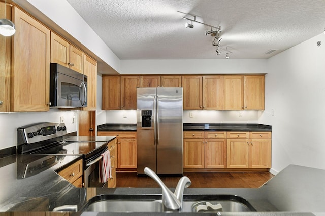 kitchen featuring appliances with stainless steel finishes, dark wood finished floors, a sink, and a textured ceiling