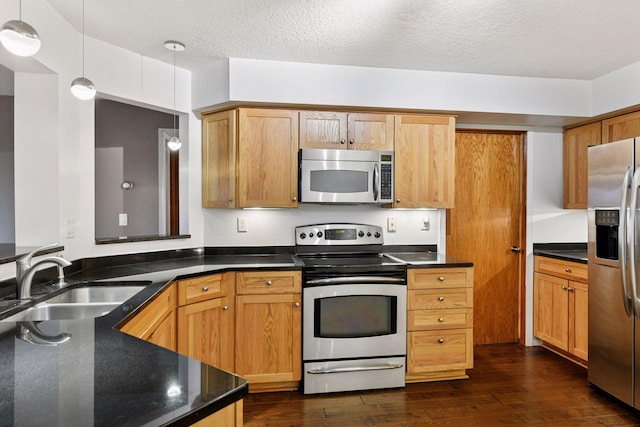 kitchen with pendant lighting, appliances with stainless steel finishes, dark wood-type flooring, a sink, and a textured ceiling