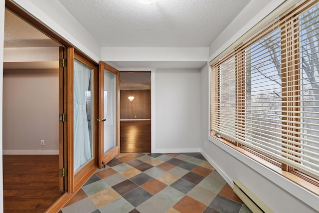 corridor with dark floors, baseboards, baseboard heating, and a textured ceiling