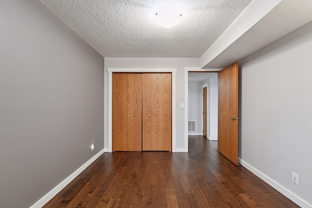 unfurnished bedroom featuring dark wood-style flooring, visible vents, a textured ceiling, and baseboards