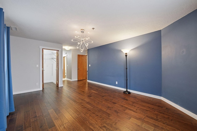 empty room with a chandelier, dark wood-style flooring, visible vents, and baseboards