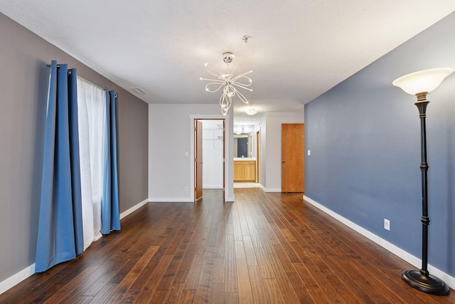 empty room featuring baseboards, visible vents, dark wood finished floors, and a notable chandelier