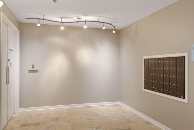 empty room with rail lighting, stone finish flooring, baseboards, and mail area