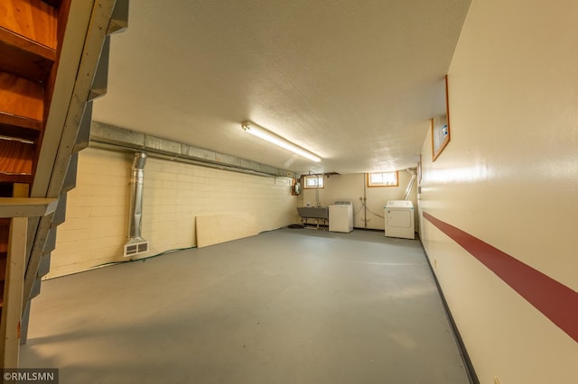 basement featuring a textured ceiling, separate washer and dryer, a sink, and concrete block wall