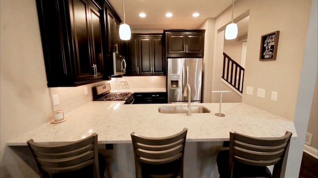 kitchen with appliances with stainless steel finishes, a sink, a peninsula, and dark brown cabinets