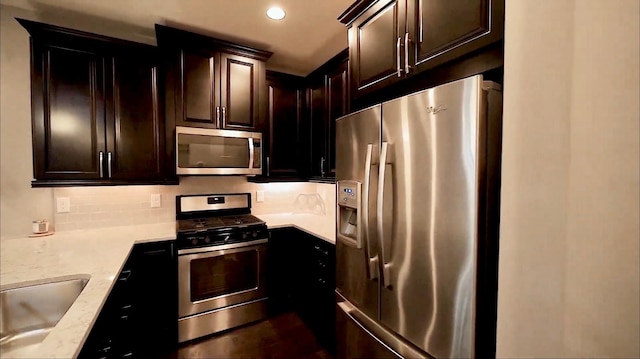 kitchen featuring recessed lighting, stainless steel appliances, a sink, dark brown cabinets, and tasteful backsplash