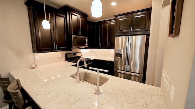 kitchen featuring decorative backsplash, appliances with stainless steel finishes, hanging light fixtures, light stone countertops, and a sink