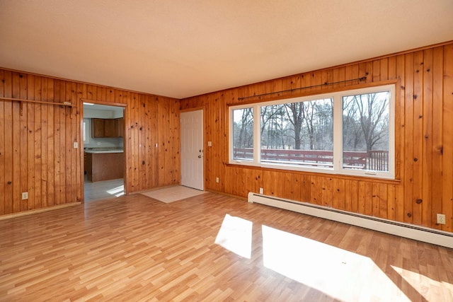 unfurnished room with a baseboard heating unit, wooden walls, and wood finished floors