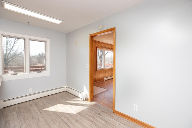 empty room featuring baseboard heating, light wood-style flooring, a baseboard heating unit, and wooden walls