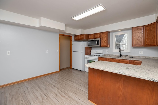 kitchen featuring brown cabinetry, white appliances, a peninsula, and a sink