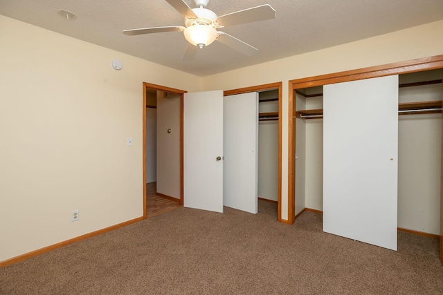 unfurnished bedroom with carpet flooring, a textured ceiling, two closets, and baseboards