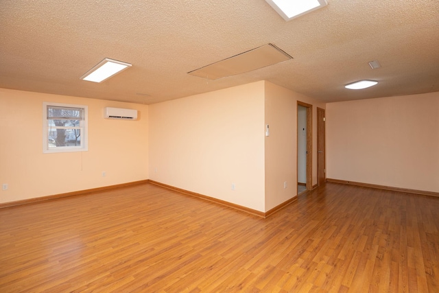 spare room with light wood-style flooring, a textured ceiling, and a wall mounted air conditioner