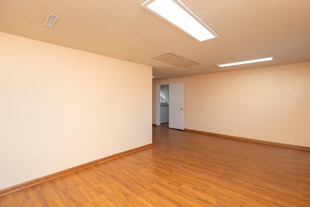 unfurnished room featuring visible vents, light wood-style flooring, washer / clothes dryer, a textured ceiling, and baseboards