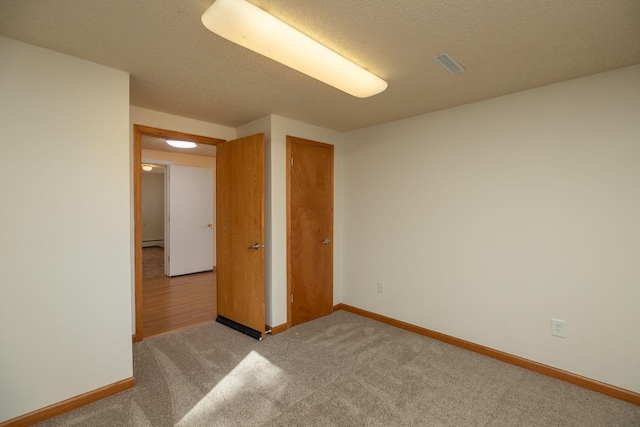 spare room with visible vents, light colored carpet, a textured ceiling, and baseboards