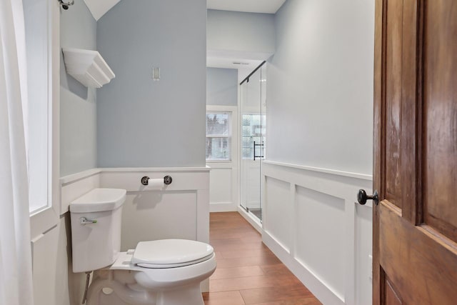 bathroom featuring toilet, a decorative wall, wood finished floors, wainscoting, and a stall shower