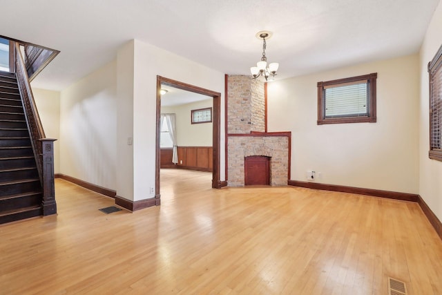 unfurnished living room with visible vents, light wood-style flooring, stairs, a fireplace, and a chandelier