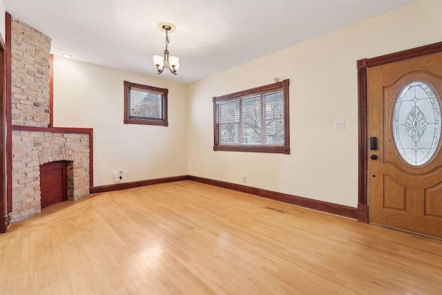 unfurnished living room with a brick fireplace, baseboards, light wood finished floors, and a notable chandelier