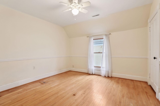 additional living space with light wood finished floors, visible vents, a ceiling fan, vaulted ceiling, and baseboards