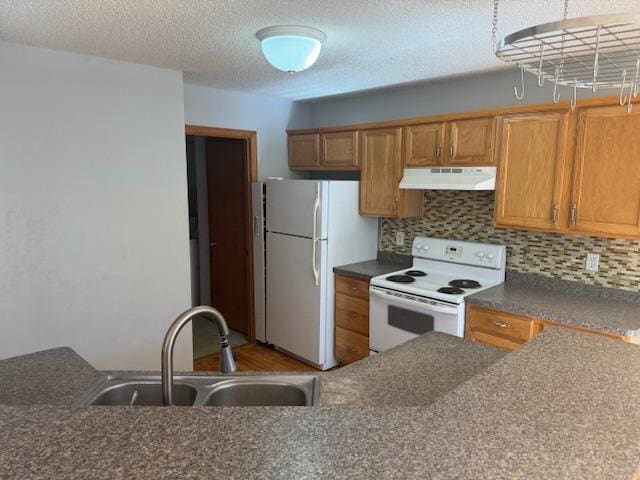 kitchen with dark countertops, white appliances, a sink, and under cabinet range hood