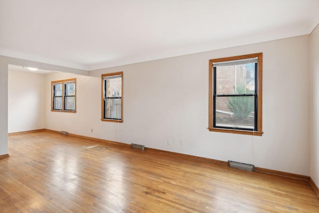 spare room with light wood-type flooring, visible vents, and baseboards