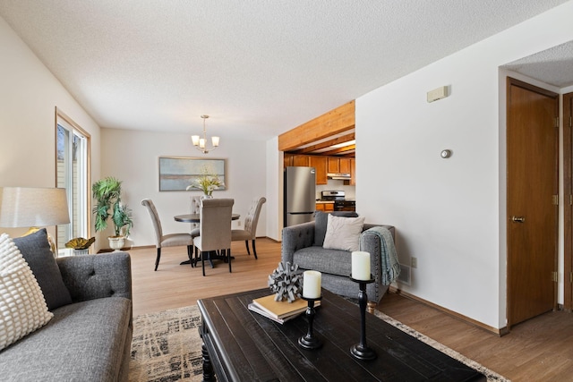 living area featuring a textured ceiling, light wood finished floors, a chandelier, and baseboards