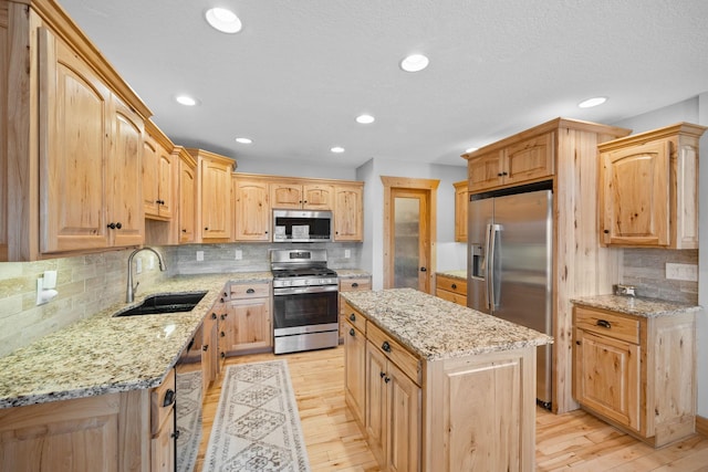 kitchen featuring light stone counters, appliances with stainless steel finishes, a sink, a kitchen island, and light wood-type flooring