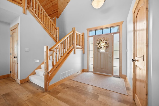 foyer featuring baseboards, visible vents, a towering ceiling, hardwood / wood-style flooring, and stairs