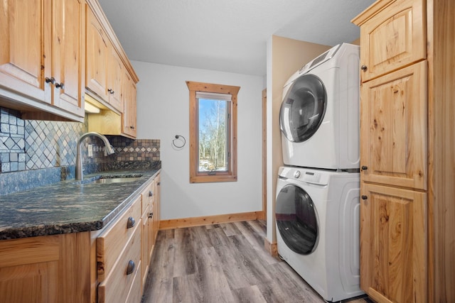 laundry area with cabinet space, baseboards, light wood-style floors, stacked washing maching and dryer, and a sink