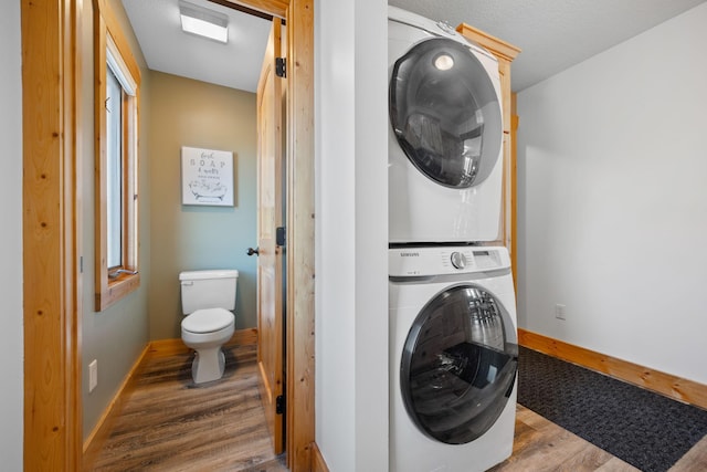 clothes washing area with laundry area, baseboards, stacked washer / drying machine, and wood finished floors