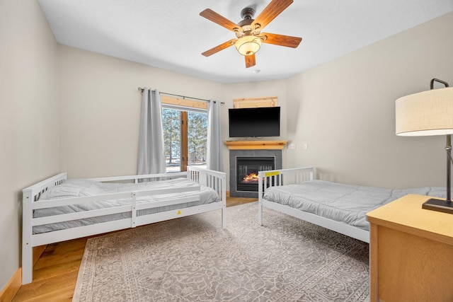 bedroom featuring baseboards, a tiled fireplace, a ceiling fan, and wood finished floors