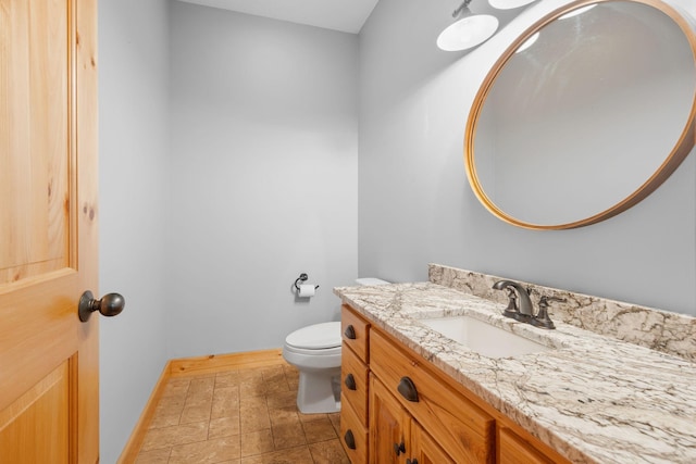 half bathroom with vanity, toilet, and baseboards