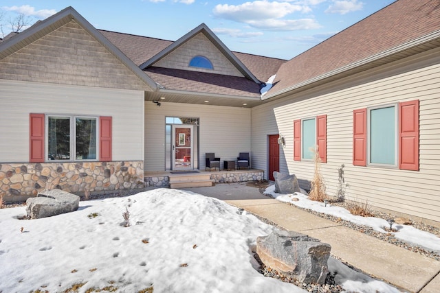 view of front of property featuring stone siding, covered porch, and roof with shingles