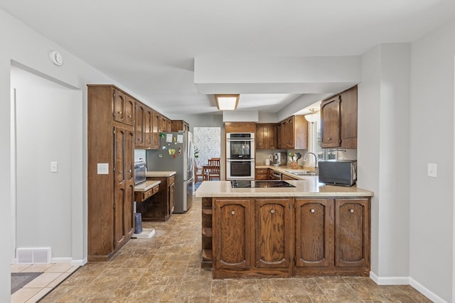 kitchen featuring visible vents, a peninsula, stainless steel appliances, light countertops, and a sink