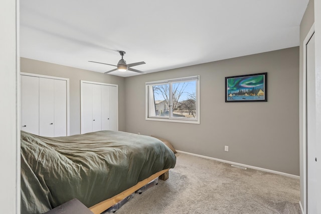 carpeted bedroom with ceiling fan, two closets, and baseboards