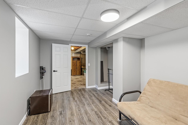 living area with a drop ceiling, baseboards, and wood finished floors