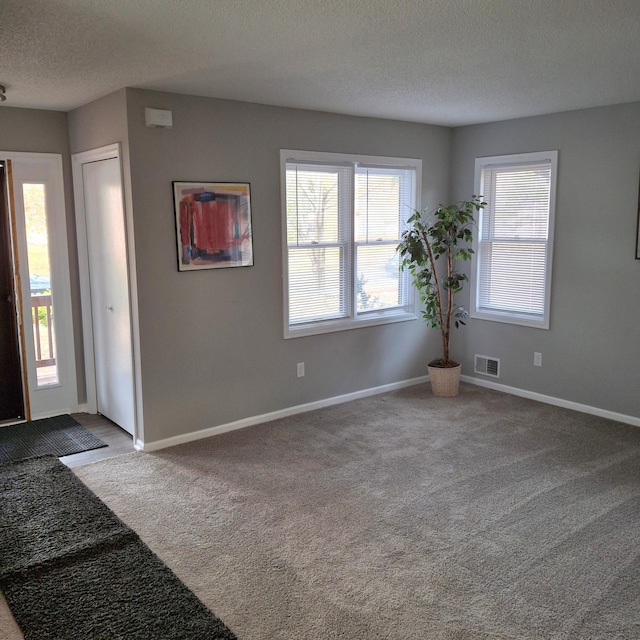 carpeted foyer featuring visible vents, baseboards, and a textured ceiling