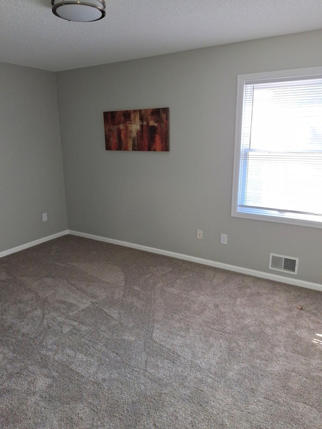 carpeted spare room featuring baseboards, visible vents, and a textured ceiling