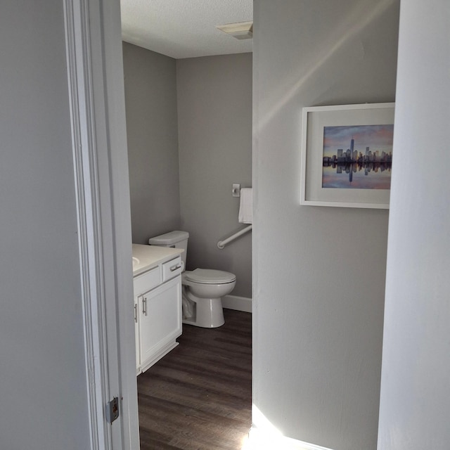 half bathroom featuring baseboards, toilet, vanity, wood finished floors, and a textured ceiling