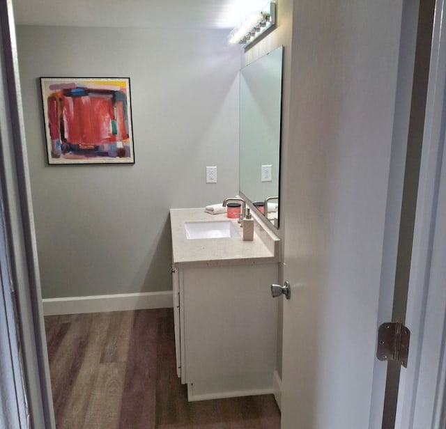 half bath with vanity, wood finished floors, and baseboards