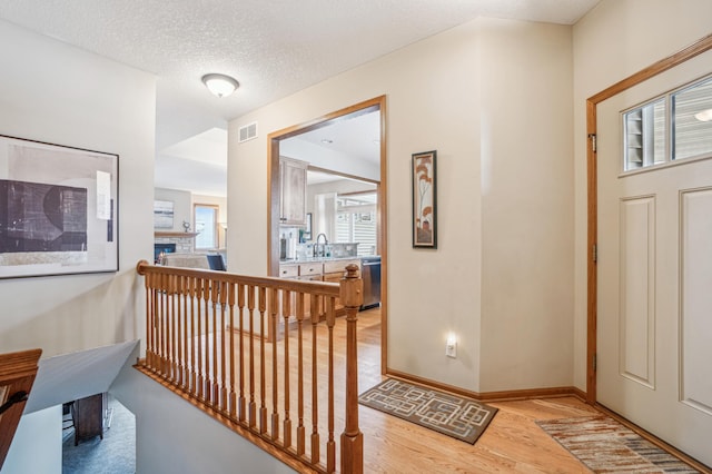 entrance foyer with a textured ceiling, visible vents, baseboards, a glass covered fireplace, and light wood-style floors