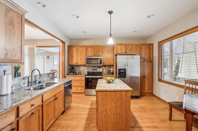 kitchen with appliances with stainless steel finishes, a sink, light wood-style floors, a center island, and backsplash