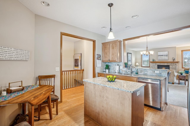 kitchen featuring a kitchen island, stainless steel dishwasher, a sink, open floor plan, and light wood-style flooring